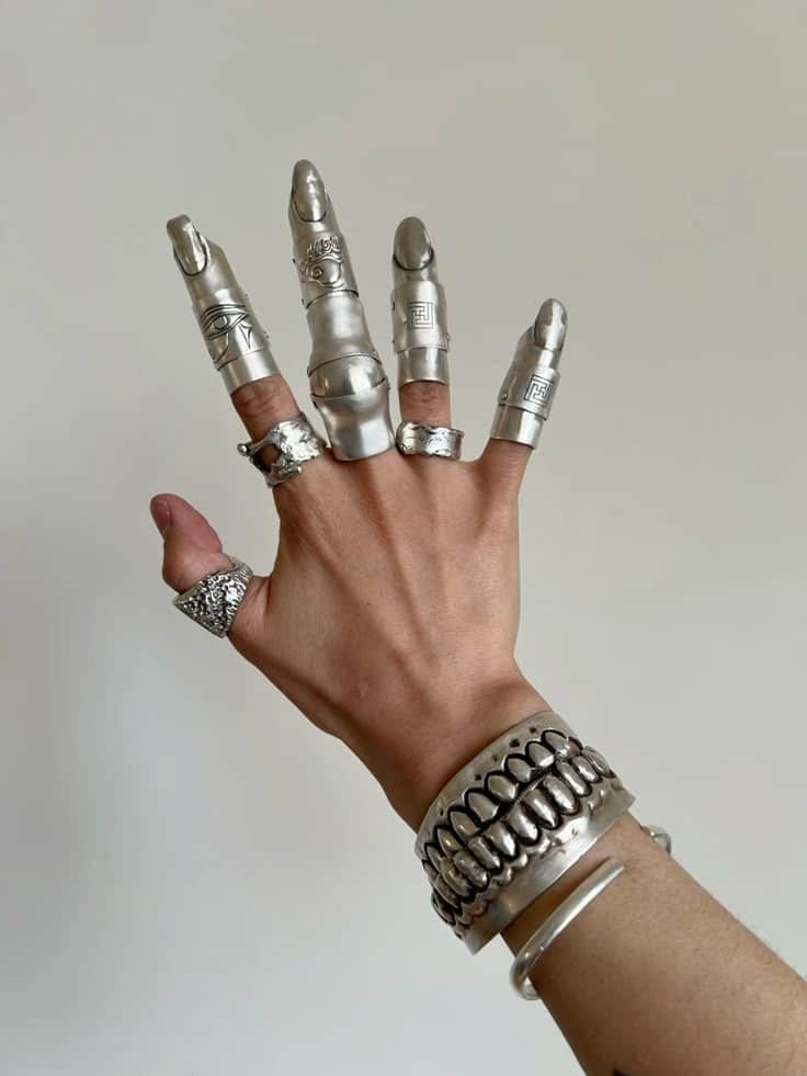 A hand wearing a wide silver cuff and individual silver finger armor caps with carved symbols.