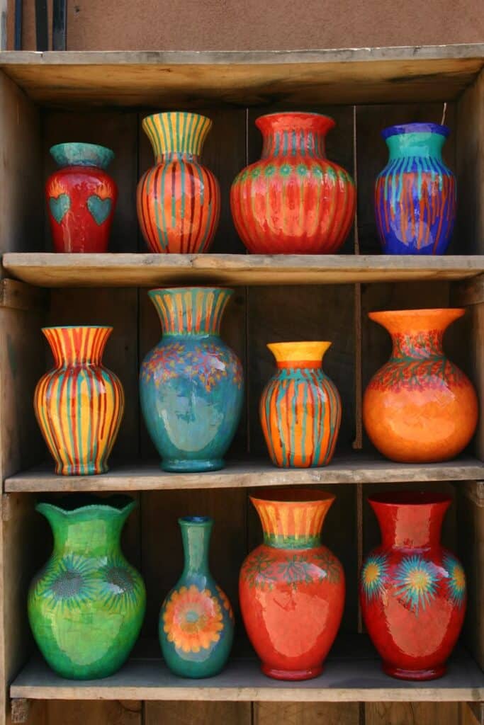 Display of twelve brightly colored, hand-painted ceramic vases on wooden shelves.